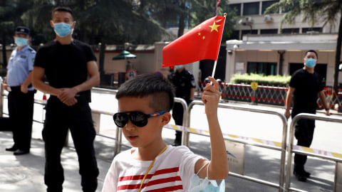 Seorang anak memegang bendera China berdiri di seberang jalan Konsulat Jenderal Amerika Serikat di Chengdu, China. Foto: Thomas Peter/REUTERS