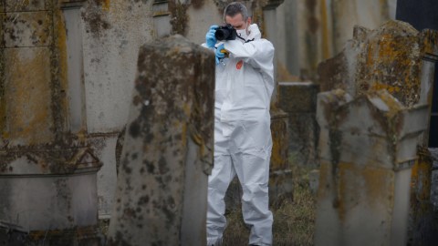 Seorang petugas melakukan penyelidikan dengan memotret makam yang dinodai dengan swastika di pemakaman Yahudi di Quatzenheim, Prancis. Foto: REUTERS/Vincent Kessler