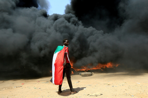 Seseorang yang mengenakan bendera Sudan berdiri di depan tumpukan ban yang terbakar selama protes terhadap prospek pemerintahan militer di Khartoum. Foto: MOHAMED NURELDIN ABDALLAH/REUTERS