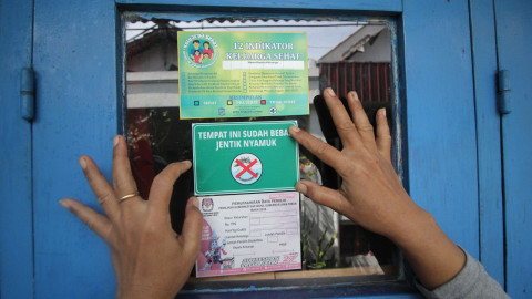 Seorang kader Ibu Memantau Jentik (Bumantik) menempelkan stiker bebas jentik nyamuk di salah satu rumah warga saat Gerakan Pemberantasan Sarang Nyamuk. Foto: Antara/Moch Asim