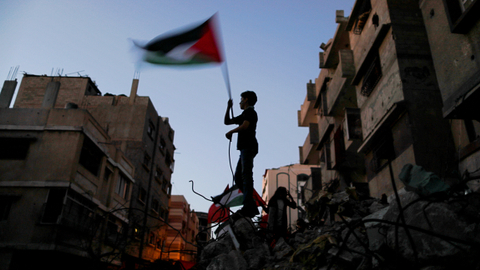 Seorang anak laki-laki mengibarkan bendera Palestina di sebuah bangunan rusak, di Gaza, Minggu (23/5) Foto: Suhaib Salem/REUTERS
