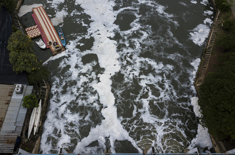 Foto: Warga Cari Ikan di Kanal Banjir Timur yang Diselimuti Limbah Berbusa