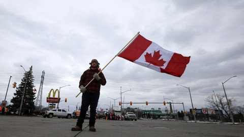 Seseorang mengibarkan bendera Kanada saat Jembatan yang menghubungkan Detroit dan Windsor ditutup secara efektif setelah pengemudi truk dan pendukung mereka memblokirnya sebagai protes terhadap mandat vaksin penyakit virus corona. Foto: REUTERS/Carlos Osorio
