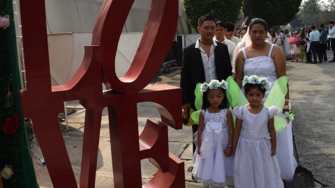 Pasangan suami istri beserta anaknya berdiri di sebelah patung huruf "LOVE" selama pernikahan massal di Manila, Filipina. Foto: AFP/TED ALJIBE