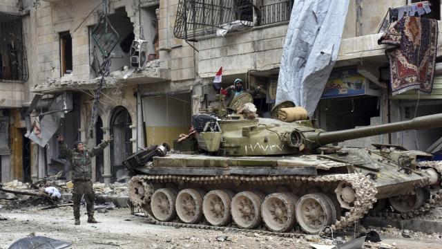 Tentara Suriah memberi tanda kemenangan dekat sebuah tank di Sukkari, Aleppo timur. (Foto: SANA via AP)