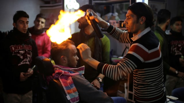 Odwan menyemprotkan api ke rambut pelanggannya. (Foto: Reuters/Ibraheem Abu Mustafa)