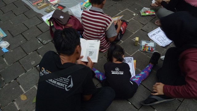 Abduh mengantarkan anak sambil membaca buku. (Foto: Ardhana Pragota/kumparan)