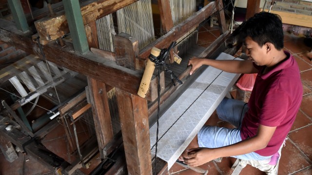 Seorang pekerja saat membuat kain dengan alat tenun. Foto:  ANTARA FOTO/Aditya Pradana Putra