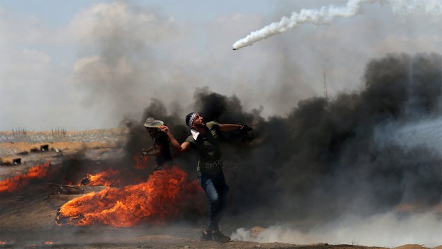 Seorang demonstran mengembalikan gas air mata. (Foto: REUTERS / Ibraheem Abu Mustafa)
