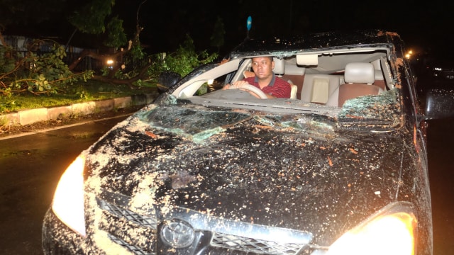Seorang warga mengendarai mobilnya yang rusak tertimpa pohon dampak angin puting beliung, di Jalan Ngumban Surbakti, Medan, Sumatera Utara. (Foto: Antara/Irsan Mulyadi)