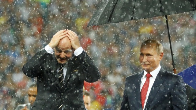 Vladimir Putin dipayungi, sementara Gianni Infantino berbasah-basahan. (Foto: Reuters/Kai Pfaffenbach)