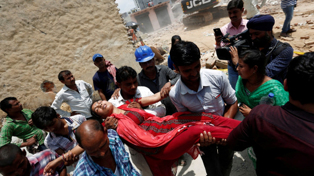 Seorang wanita, yang suaminya terperangkap di bawah reruntuhan, pingsan di lokasi bangunan perumahan yang runtuh di desa Shah Beri di Greater Noida, India. (Foto: Reuters/Adnan Abidi)
