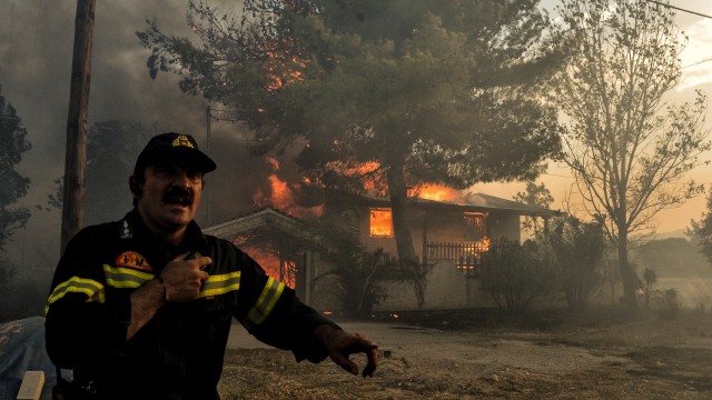 Reaksi seorang petugas ketika rumah salah satu penduduk ikut terbakar karena kebakaran hutan yang melanda di dekat area Athena, Yunani (Foto: AFP/Valerie Gache)