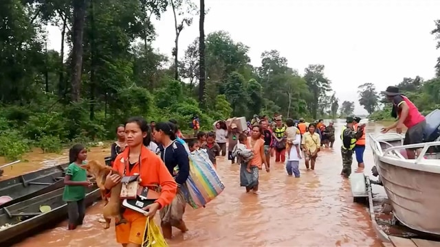 Saat penduduk desa berjalan di atas air yang membanjiri setelah perahu pengaman datang ke distrik Sanam Xay. (Foto: ATTAPEU TODAY Via REUTERS)
