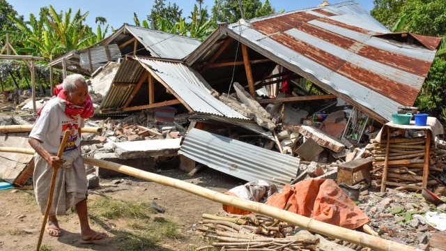 Warga berjalan di depan rumah yang roboh akibat gempa di Desa Sajang, Kecamatan Sembalun, Selong, Lombok Timur, NTB, Minggu (29/7). (Foto: Antara/Ahmad Subaidi)