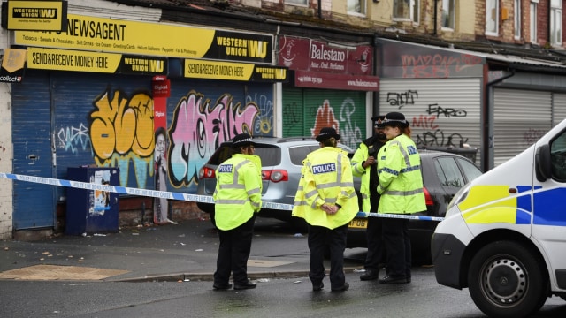 Petugas polisi berjaga-jaga di lokasi penembakan di Claremont Road di lingkungan Moss Side, Manchester, Minggu (12/8/2018). (Foto: AFP/OLI SCARFF)