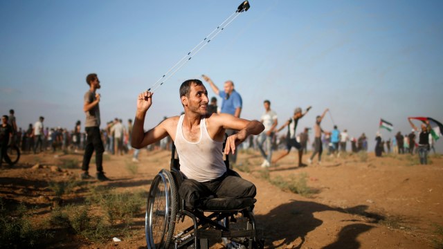 Warga difable di Palestina menggunakan ketapel untuk melemparkan batu ke pasukan Israel selama protes menuntut hak untuk kembali ke tanah air mereka di perbatasan Israel-Gaza, Jumat (17/8/2018). (Foto: Reuters/Mohammed Salem)