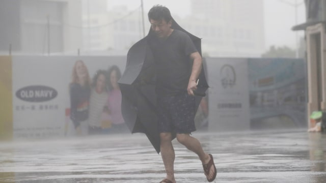 Seorang pria memegang payung sambil berjalan saat hujan deras saat Topan Mangkhut melanda, di Shenzhen, Cina, Minggu (16/9/2018). (Foto: REUTERS/Erik De Castro)