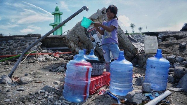 Seorang anak menampung air bersih yang keluar dari pipa saluran air pasca gempa bumi dan tsunami di Palu. (Foto: Jamal Ramadhan/kumparan)