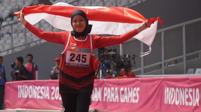Karisma Evi Tiarani mengibarkan bendera usai menyabet medali emas di nomor lari 100 meter kategori T42/63 di Asian Para Games 2018. (Foto: Irfan Adi Saputra/kumparan)