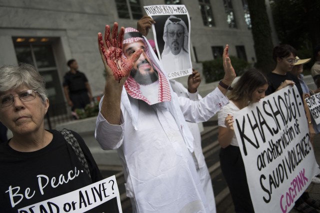 Seorang pengunjuk rasa berpakaian seperti Pangeran Arab Saudi, Mohammed bin Salman (tengah), dengan tangan yang diwarnai darah. (Foto: AFP/JIM WATSON)