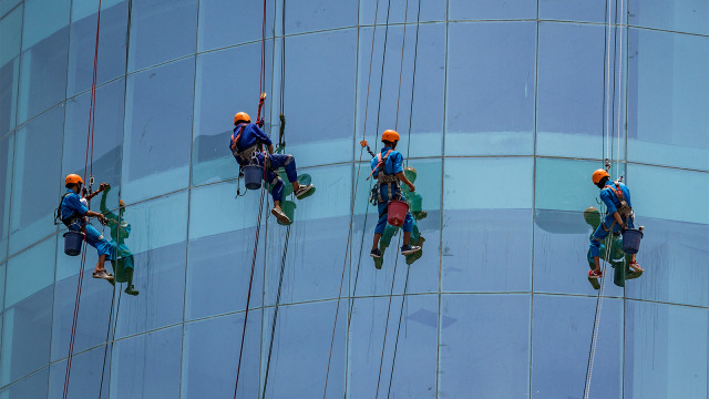 Sejumlah pekerja mengenakan alat pelindung diri (APD) saat membersihkan kaca sebuah gedung. Foto: ANTARA FOTO/Aji Styawan