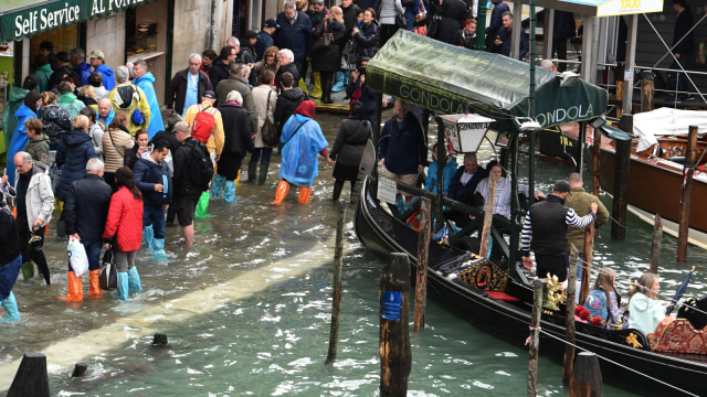 Orang-orang berjalan di atas jembatan gantung di St Mark Square yang terkena banjir di Venesia. (Foto: AFP/Miguel MEDINA)