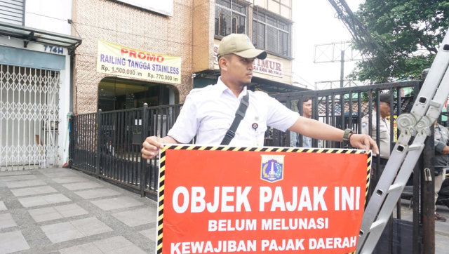 Petugas Badan Pajak dan Retribusi Daerah (BPRD) DKI Jakarta memasang tanda stiker penunggak pajak didaerah DKI Jakarta, Rabu (7/11/2018). (Foto: Helmi Afandi Abdullah/kumparan)
