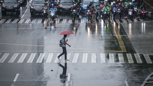 Seorang warga menggunakan payung menyeberangi jalan saat hujan di kawasan Jalan MH Thamrin, Jakarta. Foto: ANTARA FOTO/Aprillio Akbar