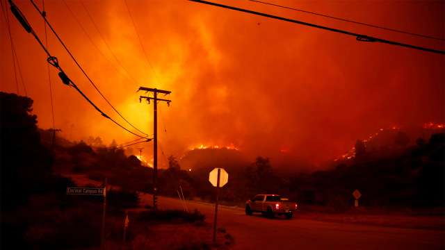 Sebuah kendaraan melintasi kawasan hutan dan rumah penduduk yang terbakar di kawasan Malibu, California, AS. (Foto: REUTERS / Eric Thayer)