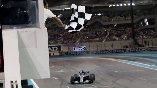 Aktor Will Smith mengibarkan bendera finis ketika Hamilton menjadi pemenang di GP Abu Dhabi. (Foto: Luca Bruno/Pool via REUTERS)