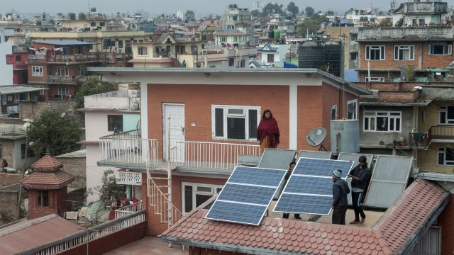 Petugas memperbaiki panel surya di atap rumah warga. (Foto: Bikash Karki / AFP)