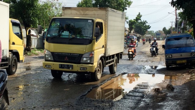 Jalan berlubang dan digenangi air membuat para pengendara memperlambat laju kendaraannya ketika melewati Jalan Mercedes Benz, Bogor. (Foto: Muhammad Lutfan Darmawan/kumparan)