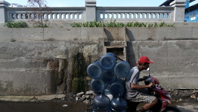 Seorang warga melintasi tanggul pengaman pantai yang bocor di kawasan Muara Baru, Jakarta. (Foto: Nugroho Sejati/kumparan)