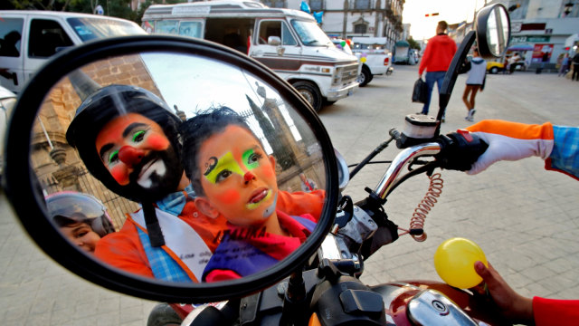 Seorang ayah dan anak mengendarai motor dalam  memperingati  International Clown Day di Guadalajara, Meksiko. (Foto: AFP/Ulises Ruiz)