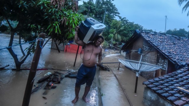 Warga membawa televisi miliknya saat banjir merendam rumahnya di kampung Kadu Gareng, Desa Sukarame, Labuan, Banten, Rabu (26/12/2018).  (Foto: ANTARA FOTO/Muhammad Adimaja)