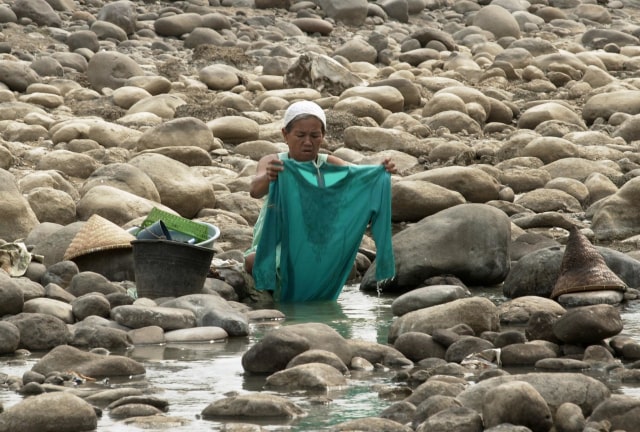 Seorang perempuan mencuci baju di pinggir kali yang mengering di Bekasi. Masalah air baru terasa oleh masyarakat ketika Indonesia masuk musim kemarau. (Foto: Weda/AFP Photo)