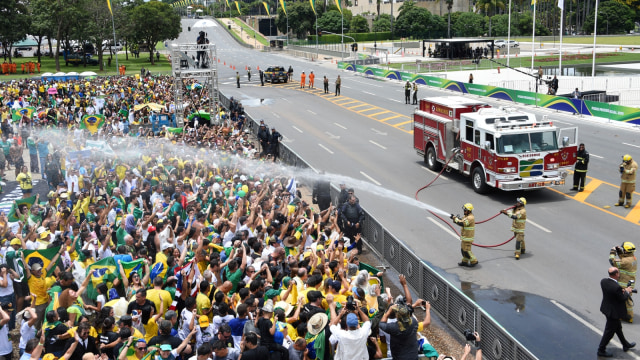 Petugas pemadam kebakaran menyemprot pendukung Presiden baru Brasil Jair Bolsonaro di Brasilia, Brasil. (Foto: AFP/EVARISTO SA)