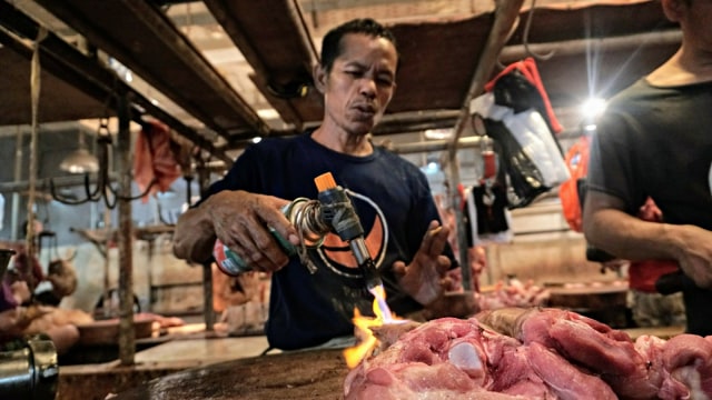 Pedagang daging babi sedang membersihkan kulit babi dari bulu rambut dengan cara dibakar. (Foto: Nugroho Sejati/kumparan)