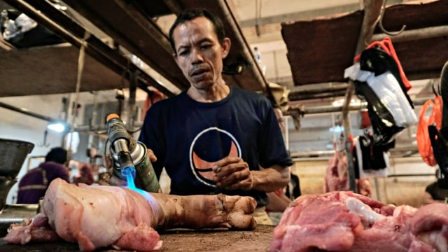 Pedagang daging babi sedang membersihkan kulit babi dari bulu rambut dengan cara dibakar. (Foto: Nugroho Sejati/kumparan)