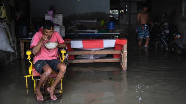 Seorang warga sedang menyantap makanannya di tengah banjir yang memasuki wilayah rumahnya setelah badai pabuk menerjang di kawasan Nakhon Si Thammarat, Thailand (5/6/2019). (Foto: AFP/Lillian SUWANRUMPHA)
