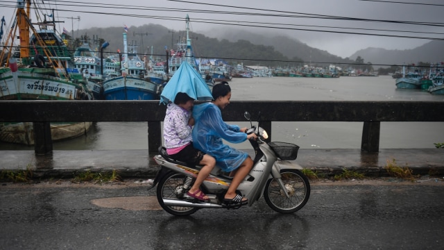 Dua orang perempuan sedang mengendarai motor di tengah hujan deras yang berada di wilayah Nakhon Si Thammarat, Thailand (5/6/2019). (Foto: AFP/Lillian SUWANRUMPHA)