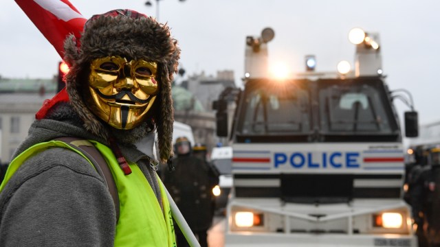 Seorang demonstran "Rompi Kuning" memakai topeng berdiri dihadapan mobil polisi Paris, Prancis, pada Sabtu (5/1/2019) (Foto: AFP/Bertrand GUAY)