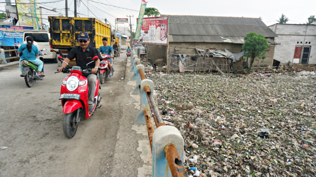 Pengendara motor melintasi hamparan sampah disertai bau menyengat yang ditimbulkan oleh penupukan sampah di Kali Pisang Batu, Bekasi. (Foto: Iqbal Firdaus/kumparan)