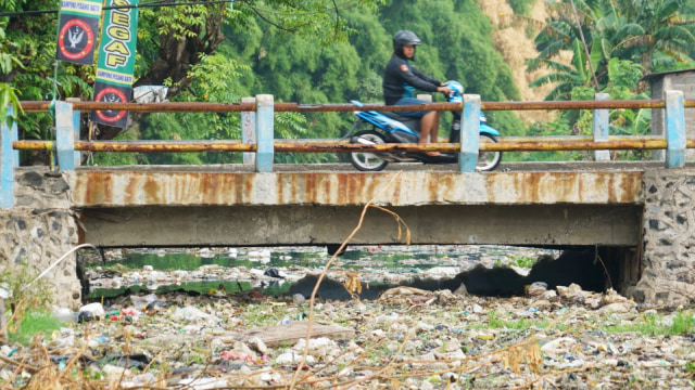 Pengendara motor melintasi hamparan sampah disertai bau menyengat yang ditimbulkan oleh penupukan sampah di Kali Pisang Batu, Bekasi. (Foto: Iqbal Firdaus/kumparan)