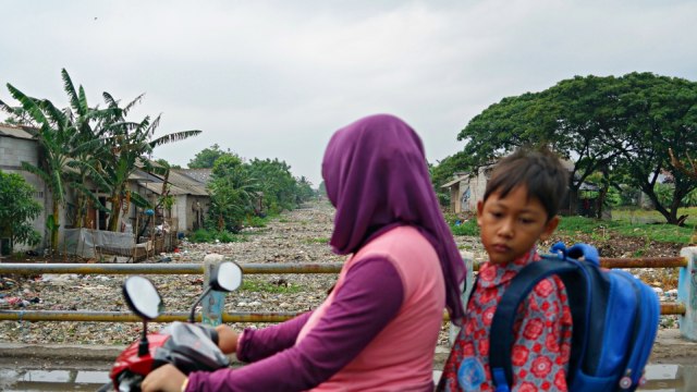 Pengendara motor melintasi hamparan sampah disertai bau menyengat yang ditimbulkan oleh penupukan sampah di Kali Pisang Batu, Bekasi. (Foto: Iqbal Firdaus/kumparan)