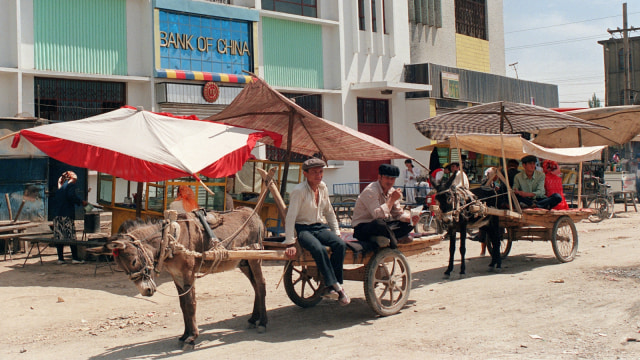 Pekerja Uighur bersantai di kereta kuda milik mereka di dekat Bank of China di Kuqa sebuah desa kecil, di barat laut provinsi Xinjiang Cina. (Foto: AFP/PHILIPPE MASSONNET)