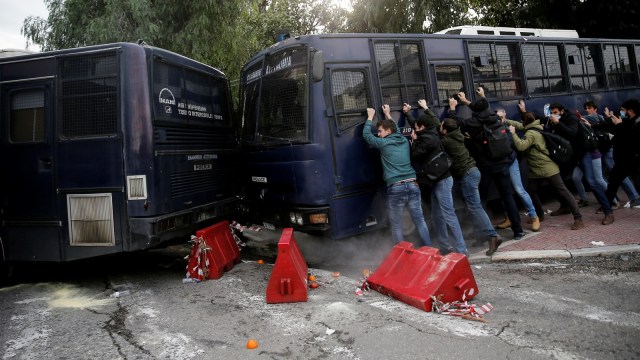 Para pengunjuk rasa mendorong bus polisi ketika para guru sekolah Yunani bentrok dengan polisi anti huru hara selama demonstrasi. (Foto: Reuters/Costas Baltas)