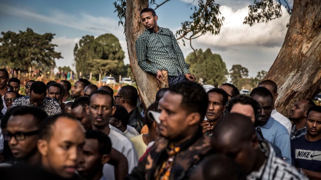 Seorang pria diatas pohon melihat pemakaman korban ledakan bom dan baku tembak komplek perkantoran dan hotel di Nairobi, (16/1/19).  (Foto: AFP/Luis TATO)