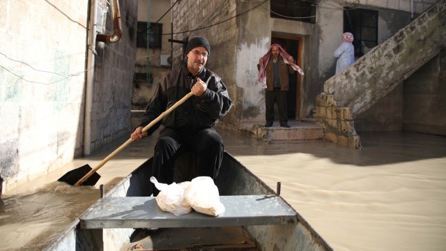 Abu Ihab mendayung perahu kecil di sepanjang jalan yang banjir membawa tas roti pipih untuk dikirimkan kepada penduduk yang terlantar di kota Darkush. (Foto: AFP/Aaref WATAD)